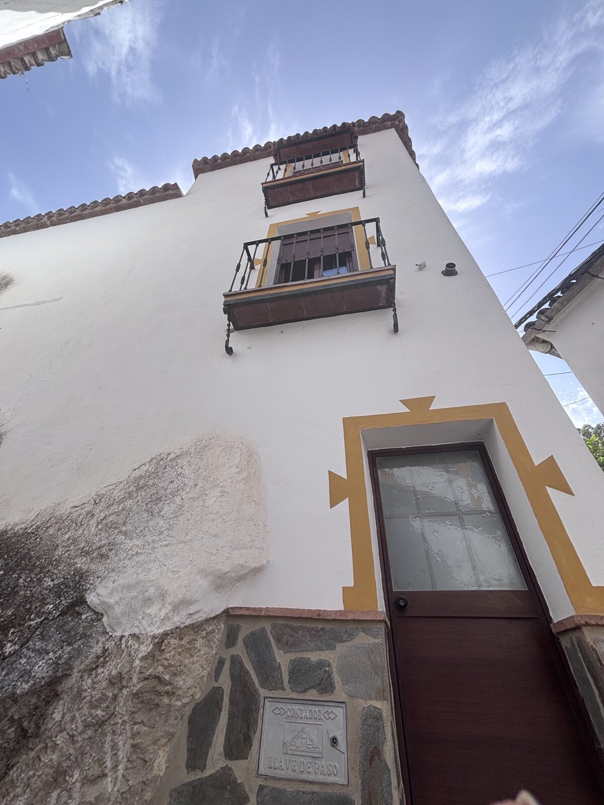 Fachada encalada con balcones de forja y puerta con cenefa amarilla