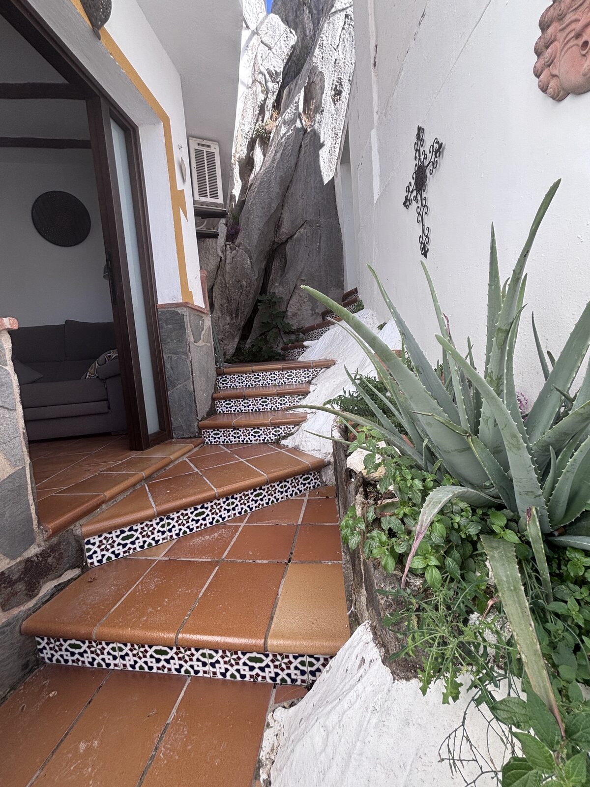 Escalones de barro y azulejo junto a la roca, con plantas de aloe