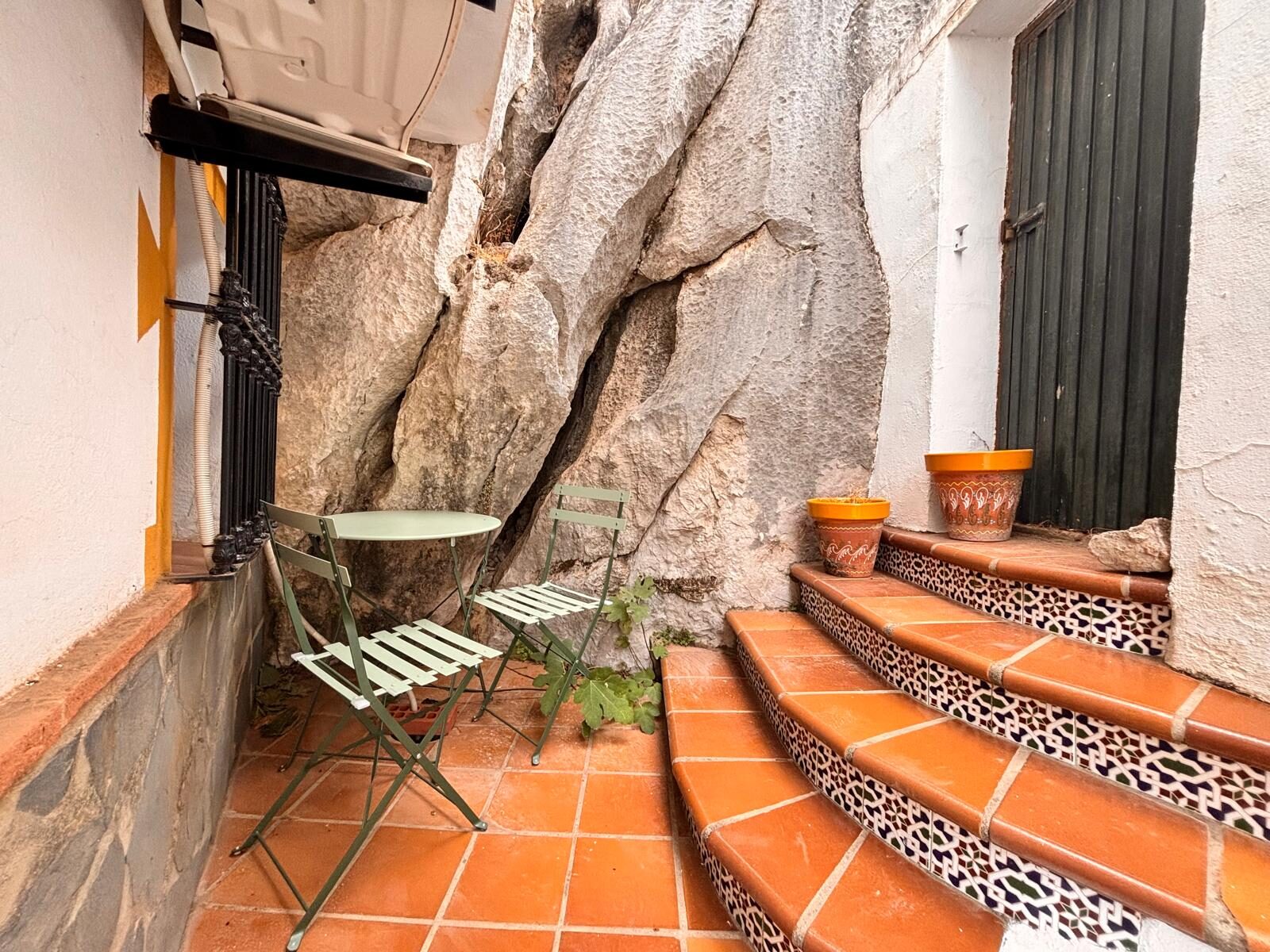 Mesa y sillas verdes junto a la roca caliza y escalones de azulejo
