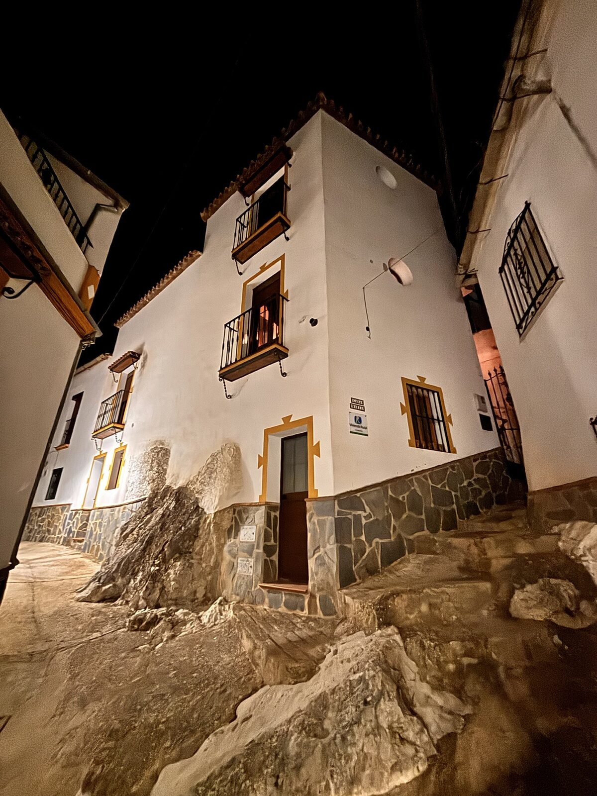 Fachada encalada de Casa Minarete iluminada de noche, junto a la roca